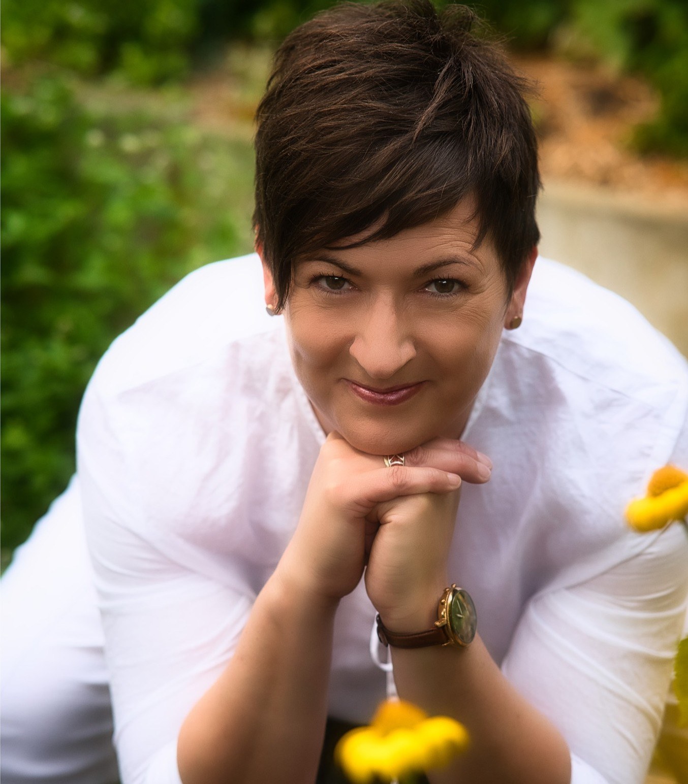 Frau im weißen Hemd, das Kinn auf die Hände gestützt, im Garten mit gelben Blumen