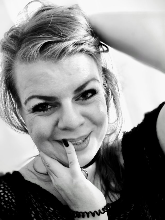 Schwarz-Weiß-Porträt einer lächelnden blonden Frau, den Finger an den Lippen