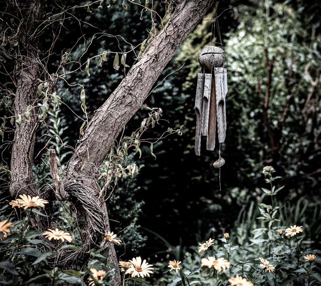 Verwunschener Gartenwinkel mit hellen Blüten und Windspiel