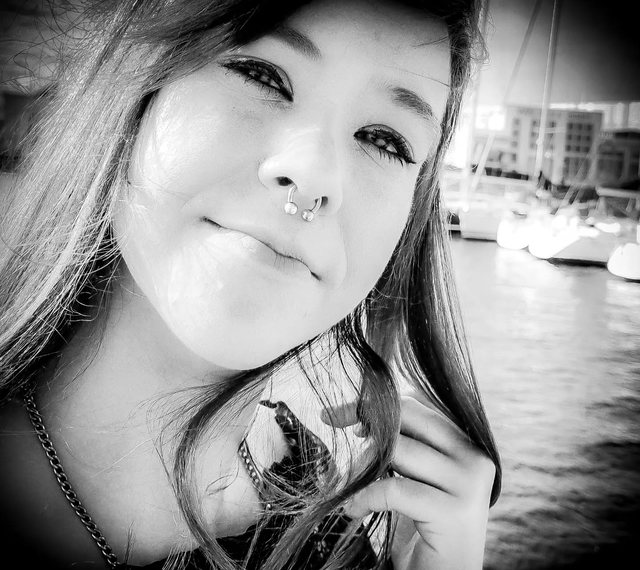 Schwarz-Weiß-Porträt einer jungen Frau am Wasser, Boote im Hintergrund