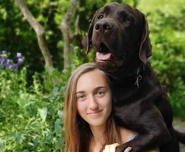 Junge Frau mit großem braunem Hund über den Schultern im Garten