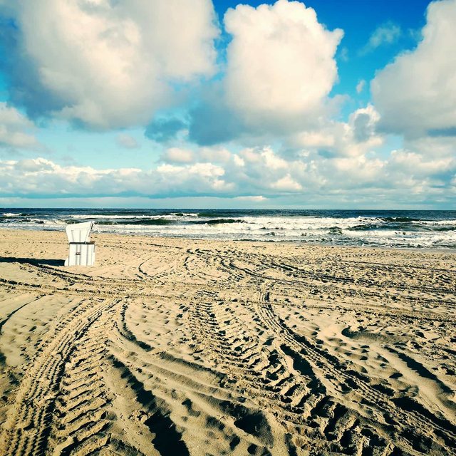 Sandstrand mit Reifenspuren unter Wolkenhimmel