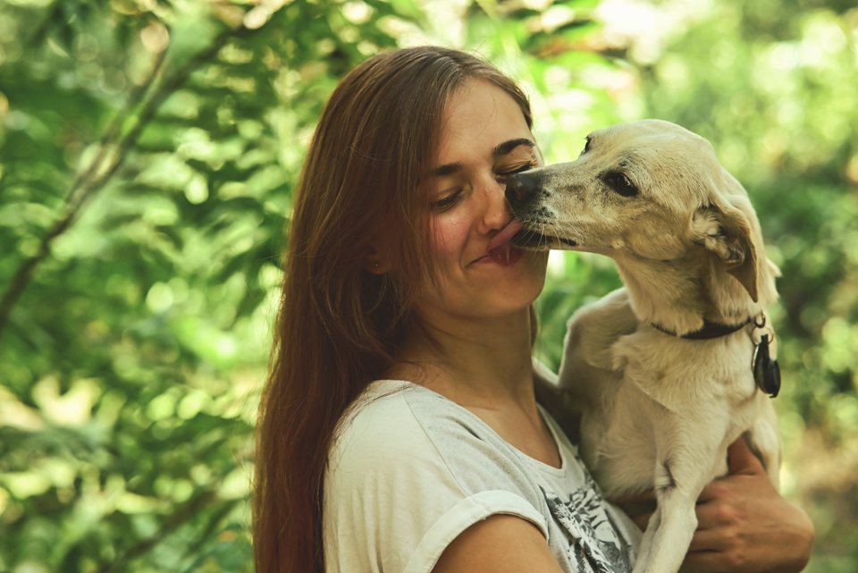 Lou hält einen hellen Hund im Arm, der ihr die Nase stupst