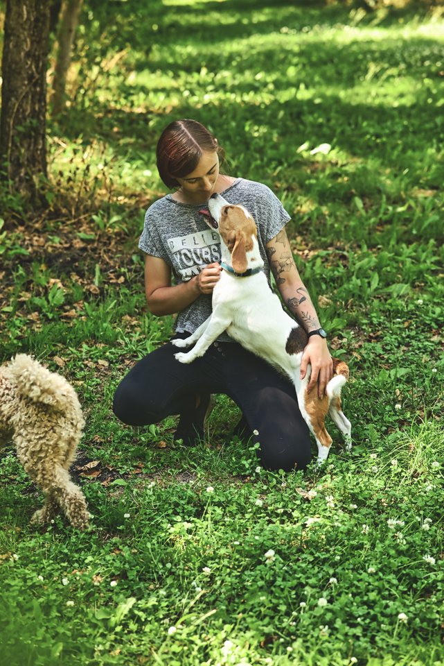 Lou kniet auf der Wiese mit einem kleinen Hund