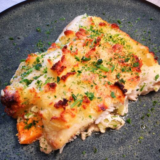 Seelachsfilet auf buntem Gemüsebett mit würziger Cremesauce und Kartoffelhaube