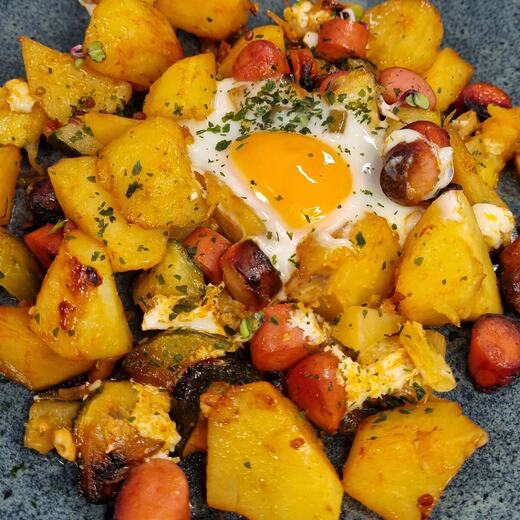 Kartoffel-Gemüsepfanne aus dem Backofen mit Würstchenscheiben und Ei