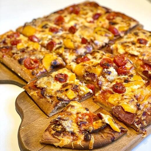 Selbstgemachte Pizza mit Wildsalami auf Vollkornteig und angerichtet auf Uromis Brettern