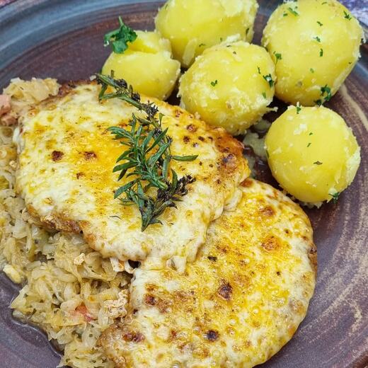 Überbackenes Schweinesteak pikant gewürzt auf deftigen Sauerkraut dazu Kräuterkartoffeln