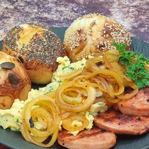 Frühstück mit Rührei, braunen Zwiebeln, gebratene Jagdwurst-Taler und frischen Brötchen