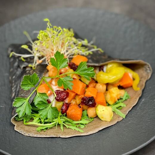 Schwarzer Wrap mit einer Füllung aus Süßkartoffeln, Kichererbsen, Zucchini, Rucola…